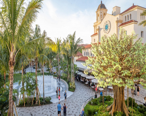 A town square with a fountain and palm trees around it and outside seating