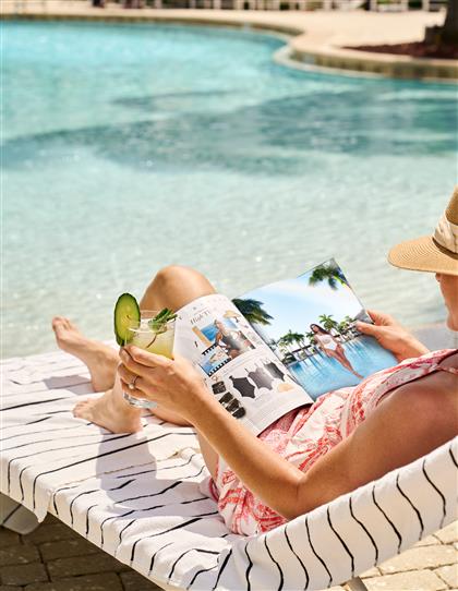 A woman reading by the pool with a drink