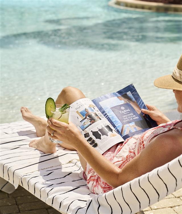 Woman sitting by the pool enjoying a cocktail and reading